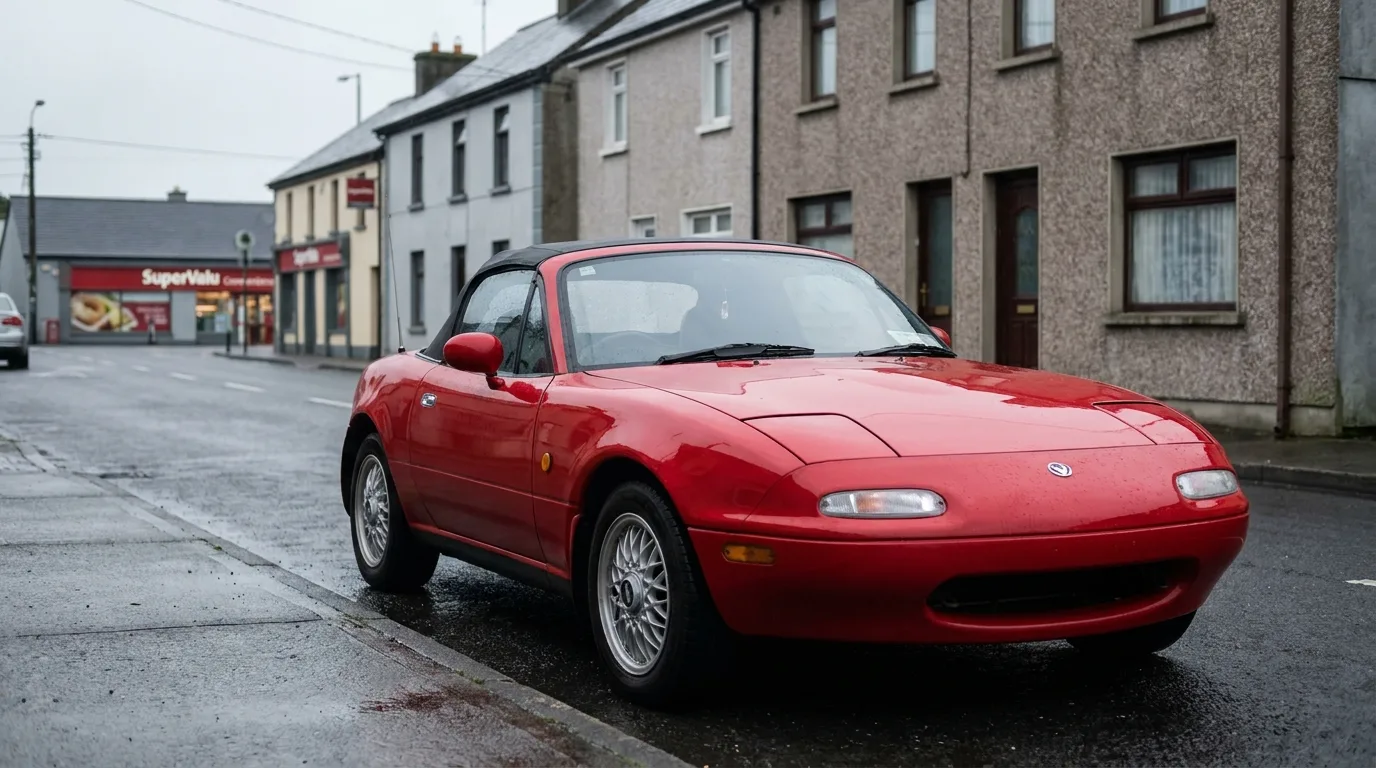 A red Mazda Eunos Roadster parked on an everyday small-town street in Ireland